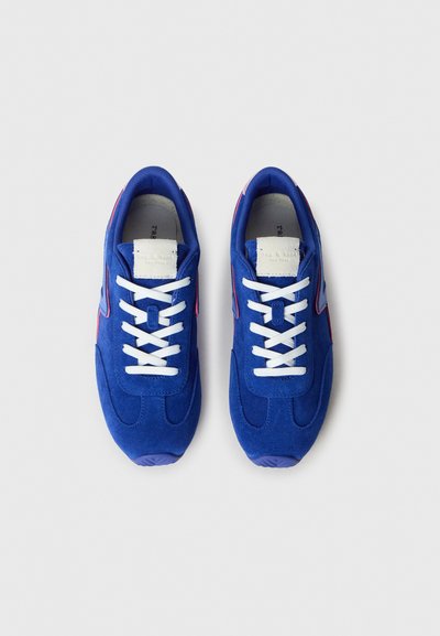 Modré semišové tenisky s bielymi šnúrkami, zaoblenou špičkou a jemnými švami. Vyznačujú sa mäkkou textúrou a kontrastnými akcentmi.