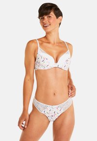 Ensemble de soutien-gorge sans fil et de culotte assortie en blanc avec des motifs de feuilles multicolores. Présente des finitions en dentelle et une texture de tissu lisse.