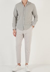 Camicia a righe bianca e verde scuro, abbinata a pantaloni slim-fit beige chiaro e sneakers bianche, il tutto su uno sfondo neutro.