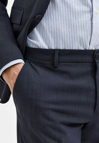 Marineblå bukser med en subtil pinstripe-design, lavet af et struktureret stof. Livremmen har diskrete løkker og en knaplukning.