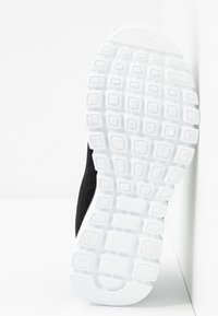 Svart sneaker sula vänd framåt, som visar en vit mönstrad gummiyttersula med fyrkantiga och rektangulära slitbanemönster.