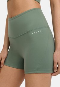 Shorts sportivi a vita alta in tessuto verde tenue, con cuciture piatte e un logo bianco in vita. Texture morbida, design aderente.