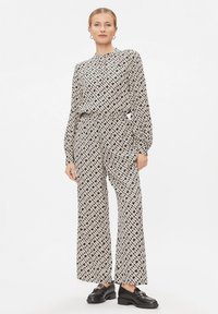 Jumpsuit a motivi bianco e nero con maniche lunghe, collo alto e pantaloni a gamba larga. Scarpe nere semplici completano il look.