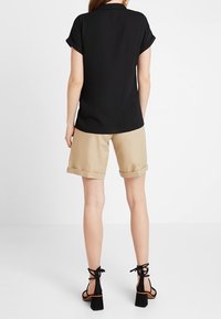 Black short-sleeved blouse with a folded cuff, paired with beige rolled shorts and black high-heeled sandals with ankle straps.