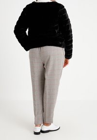 Sort jakke i imiteret pels med quiltet tekstur, kombineret med ternede bukser. Hvide sko med sorte detaljer fuldender outfittet.