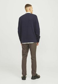 Marineblauer Strickpullover mit gerippten Bündchen und Saum, kombiniert mit braunen Hosen und schwarzen Schuhen, von hinten betrachtet.