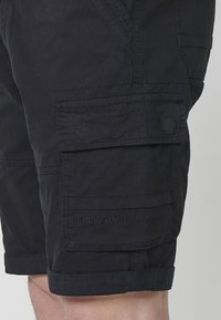 Shorts cargo noirs en tissu résistant, dotés de poches latérales, d'un ourlet retroussé et d'un détail en texte en relief sur la poche avant.