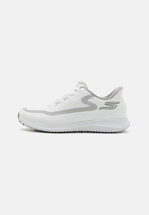 Shoe desportivo branco com um superior texturizado, detalhes em cinza, fecho de atacadores e uma sola de borracha com um padrão de tração.