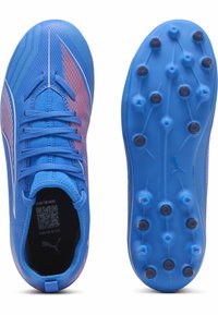 Scarpe da calcio blu con sovrastruttura testurizzata, dotate di dettagli rossi e bianchi, punta arrotondata e tacchetti modellati su una suola per terreni duri.