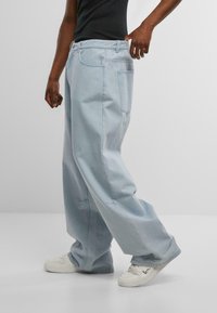 Jeans de mezclilla de corte recto, de color azul claro y de ajuste holgado. Cuentan con bolsillos tradicionales y una cinturilla estándar, combinados con zapatillas blancas.