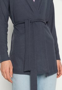 Dunkelblaue Wickelbluse mit langen Ärmeln, am Taillenbereich geknotet. Weicher Stoff mit glatter Textur und geradem Saum.