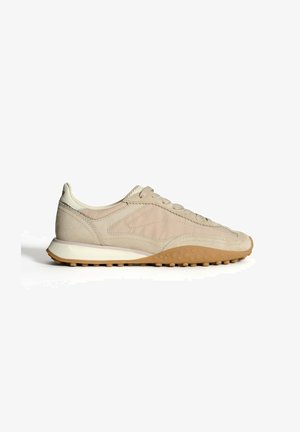 Zapatilla de ante beige con una superficie texturizada, diseño de cordones y una suela de goma ligera con pequeños agarres circulares.