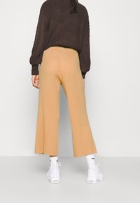 Ribbade, högmidjade beige byxor med en utsvängd silhuett, tillsammans med vita sneakers och en mörk, strukturerad stickad tröja.