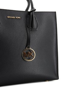 Borsa a mano in pelle nera con texture a granuli, dotata di hardware dorato, un charm staccabile con logo MK e design strutturato.