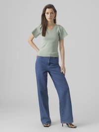 Lys grønnet tettsittende genser med korte puffermer og V-hals, kombinert med høy midje blå vide jeans og svarte stroppehæler.