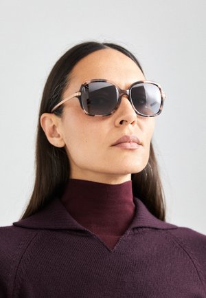 Sunglasses with a thick, hexagonal frame in a gradient of brown and light pink. Dark lenses and slender rose gold accent hardware.