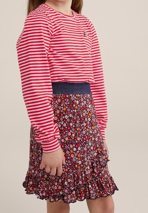 Kind trägt ein rot-weiß gestreiftes Langarmshirt und einen hoch taillierten, geblümten Rock mit Rüschen und einem dunklen Bund.