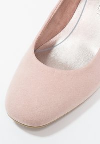 Scarpa piatta in suede rosa chiaro con punta rotonda e design a taglio. Presenta un interno liscio e metallico e una suola in gomma beige.