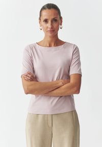 Top corto rosa chiaro con maniche corte e scollo tondo, abbinato a pantaloni beige chiaro. Tessuto morbido, texture liscia e vestibilità rilassata.