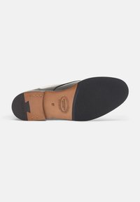 Suola di scarpa in pelle nera con una cappetta nel tacco in pelle marrone decorata con borchie dorate, fondo in gomma testurizzata e dettagli di branding impresso.