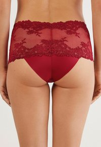 Rote Spitzen-Hipster-Unterwäsche mit einem floralen Spitzenbund und einem glatten unteren Abschnitt. Das Design betont den Kontrast zwischen den Texturen.