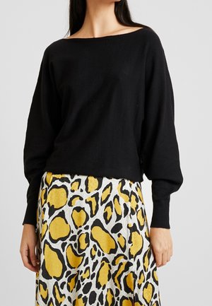 Musta, pitkähihaisuus villapaita, jossa on leveä kaula-aukko, yhdistettynä kuvioituun hameeseen, jossa on keltaisia ja mustia abstrakteja leopardipaikkoja.