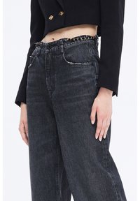 Jeans de mezclilla negro de tiro alto con un ajuste ligeramente suelto y un acento de cadena en la cintura; bolsillos frontales con detalles en costura blanca.