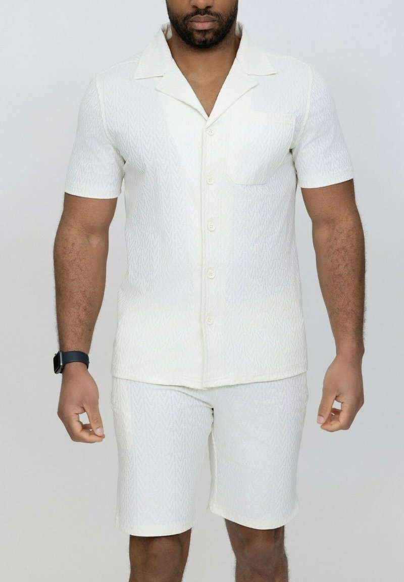 Chemise blanche à manches courtes et shorts assortis, dotés d'un motif en zigzag subtil, fabriqués en tissu léger avec une coupe décontractée.