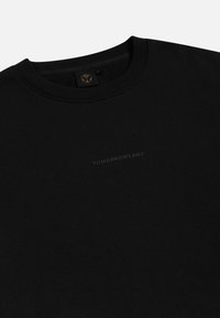 Zwarte sweatshirt met geribbelde ronde hals, zachte textuur, met een subtiele, ingedrukte "TOMORROWLAND" logo op het voorpand.