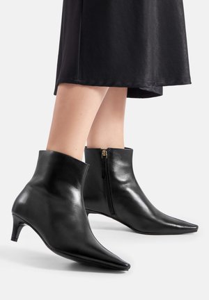 Bottes en cuir noir pour chevilles avec un bout pointu, un petit talon fin et une fermeture éclair latérale. Texture lisse et design élégant.
