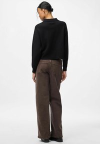 Crna kratka majica, ležernog kroja, s dugim rukavima. Uparena s smeđim širokim trapericama koje pokazuju stražnje džepove. Jednobojna, bez uzorka.