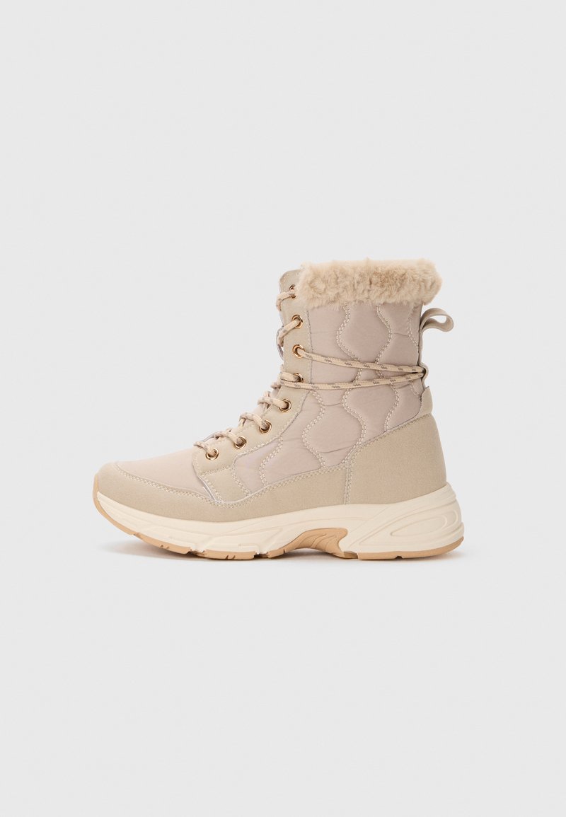 Beige vinterkänga med foder av päls, vadderad överdel, snörning i fronten och tjock texturerad sula, visad i profil på en vit bakgrund.