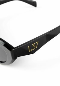 Black sunglasses with glossy frame, octagonal lenses, and gold "L37" detail on the temple, smooth texture, and contemporary design.