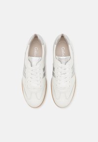 Paire de baskets en cuir blanc avec des bandes et des lacets argentés vues de dessus sur un fond clair.