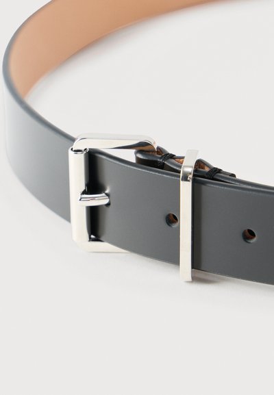 Μαύρη δερμάτινη ζώνη με ασημένια ορθογώνια αγκράφα και δύο τρύπες, τοποθετημένη σε χαλαρή σπείρα πάνω σε λευκή επιφάνεια.