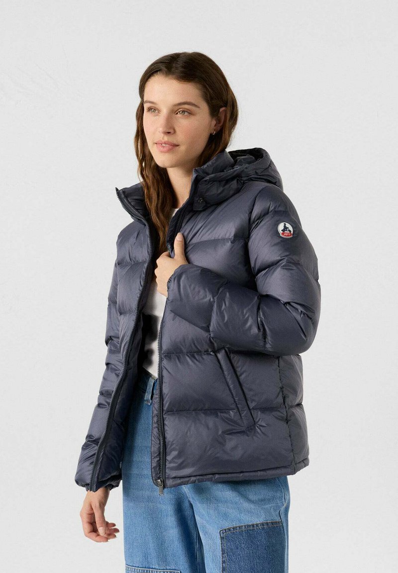 Chaqueta de abrigo azul marino con capucha, diseño acolchado y cremallera frontal. Tiene bolsillos laterales y un parche con logo en la manga izquierda.