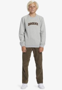 Gray sweatshirt with "QUIKSILVER" logo in dark brown, paired with olive green corduroy pants and white sneakers, standing on a white background.