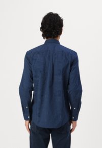 Navy blue long-sleeve shirt featuring a white polka dot pattern, classic collar, and button cuffs. Smooth fabric with a tailored fit.