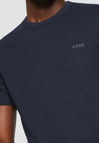 Tyrkysové tričko vyrobené z měkké bavlny, s kulatým výstřihem a krátkými rukávy; na hrudi má malé šedé logo "BOSS".