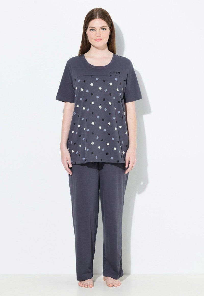 Kvinde står barfodet iført et mørkegråt pyjamas-sæt med spredte små blomsterprint og teksten "LOVE" på trøjen.