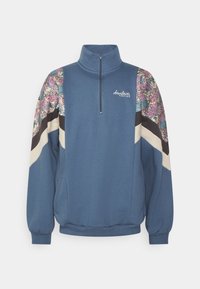 Felpa blu con colletto a mezza zip, pannelli delle spalle a motivo floreale, strisce di accento nere e beige e polsini a coste.