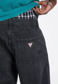 Czarne dżinsy z denimu o teksturowanej powierzchni, z triangularnym czerwono-białym logo na tylnej kieszeni oraz skórzaną metką w pasie.