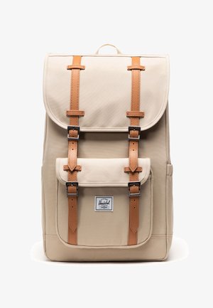 Beige canvas rugzak met bruine leren riemen en metalen gespen, voorzien van een voorvak met Herschel merklabel.