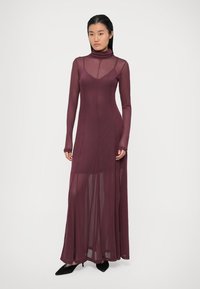 Abito lungo bordeaux a maniche lunghe con collo alto, trama trasparente, corpetto aderente e gonna fluida, con uno spacco laterale alto fino alla coscia.