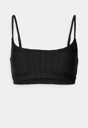 Zwarte bralette met dunne verstelbare bandjes, textuur ribbelstof en een naadloze band aan de onderkant. Geen padding of beugels zichtbaar.