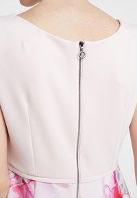 Abito senza maniche rosa chiaro con scollatura rotonda, caratterizzato da una zip argentata visibile sul retro e un motivo floreale sull'orlo.
