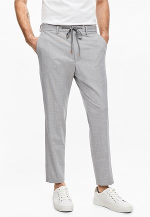 Pantaloni leggeri e grigi in tessuto intrecciato con vita a cordoncino, dotati di due tasche laterali e gambe affusolate, abbinati a sneakers bianche.