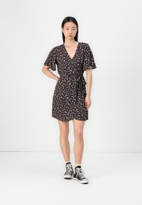 Robe ample noire à motifs floraux avec des manches courtes à volants, une taille cintrée et une jupe arrivant au genou. Portée avec des baskets montantes noires.