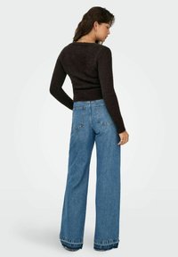 Dark brown fitted sweater with textured fabric. Worn with light blue wide-leg jeans featuring a raw hem and traditional pockets.