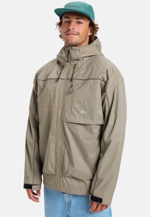 Beige wasserdichte Jacke mit durchgehendem Reißverschluss, verstellbarer Kapuze und Taschen. Mit grau genähten Nähten und elastischen Bündchen mit schwarzen Akzenten.